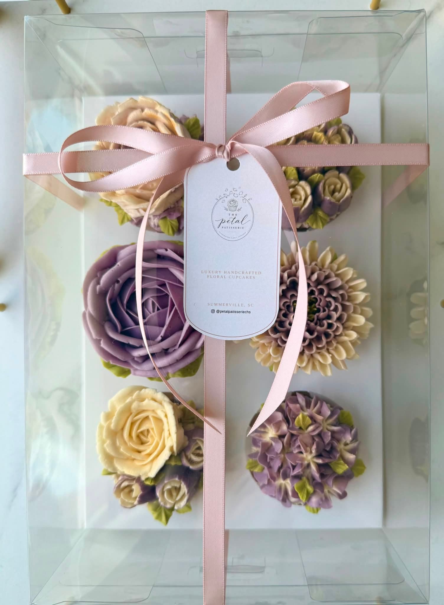 A ribbon-tied box of six floral cupcakes with lavender roses, dahlias and hydrangeas