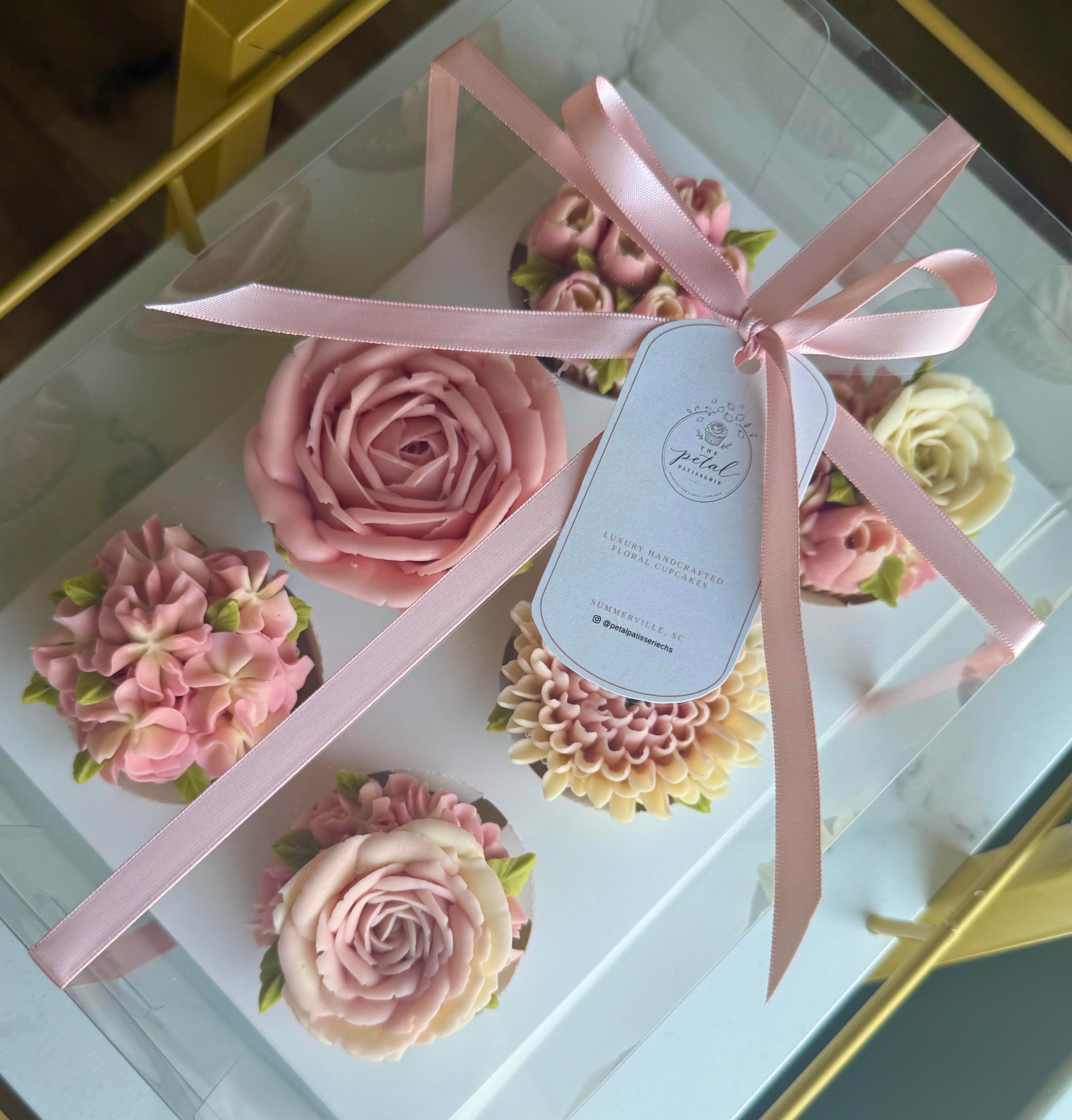 A ribbon-tied gift box of blush rose, hydrangea and dahlia cupcakes with The Petal Patisserie tag