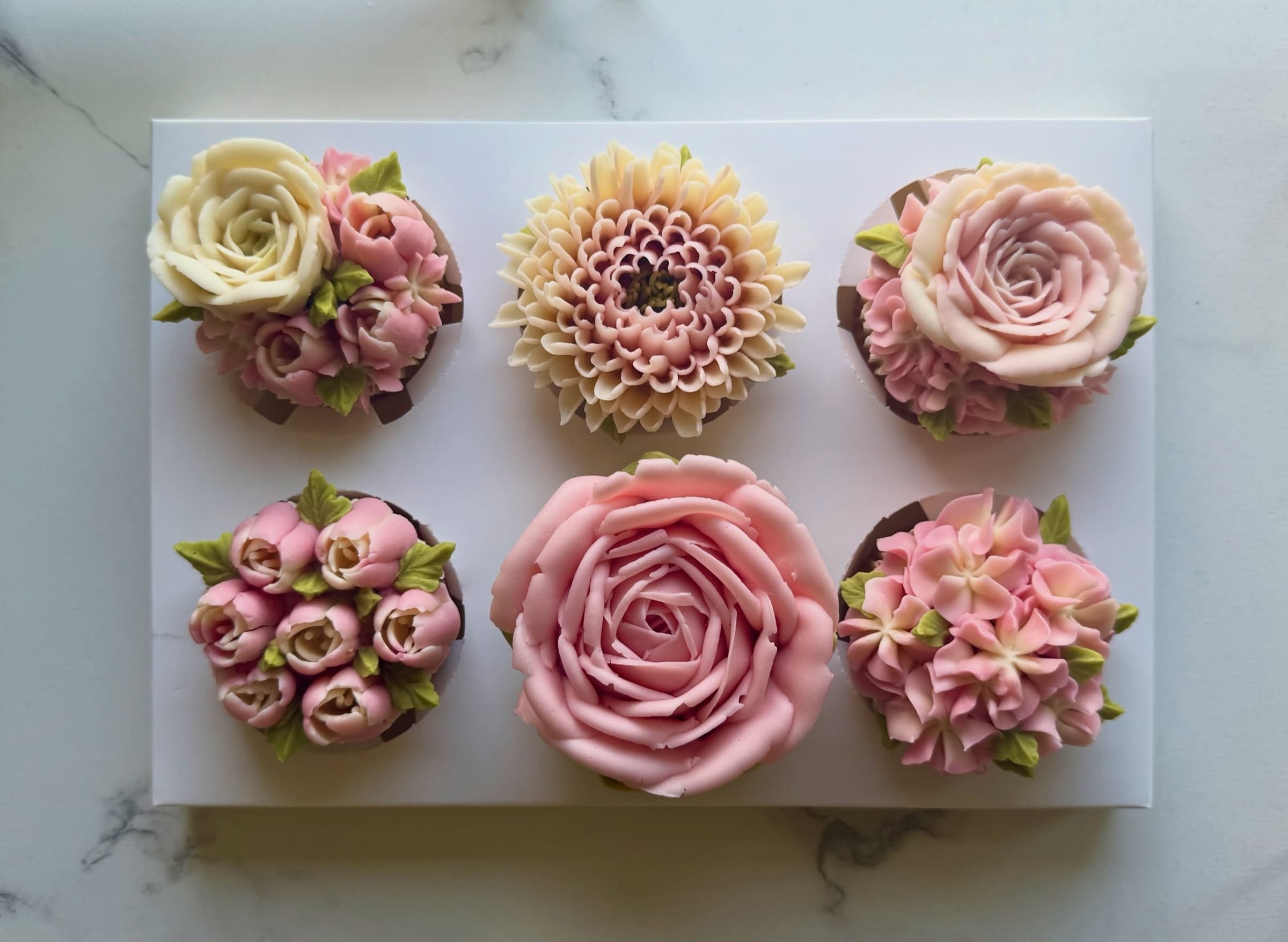 A box of six handcrafted cupcakes piped with buttercream roses, chrysanthemums, tulips and hydrangeas in blush and cream